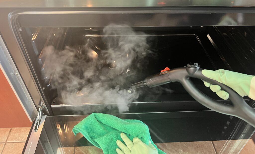 person deep cleaning a kitchen oven with steam